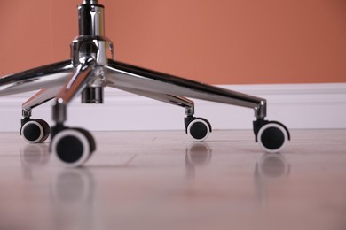 Photo of Modern office chair with wheels on wooden floor, closeup