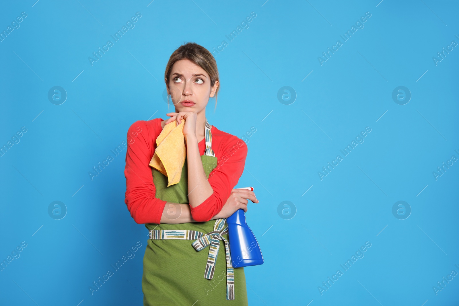 Photo of Young housewife with detergent and rag on light blue background. Space for text