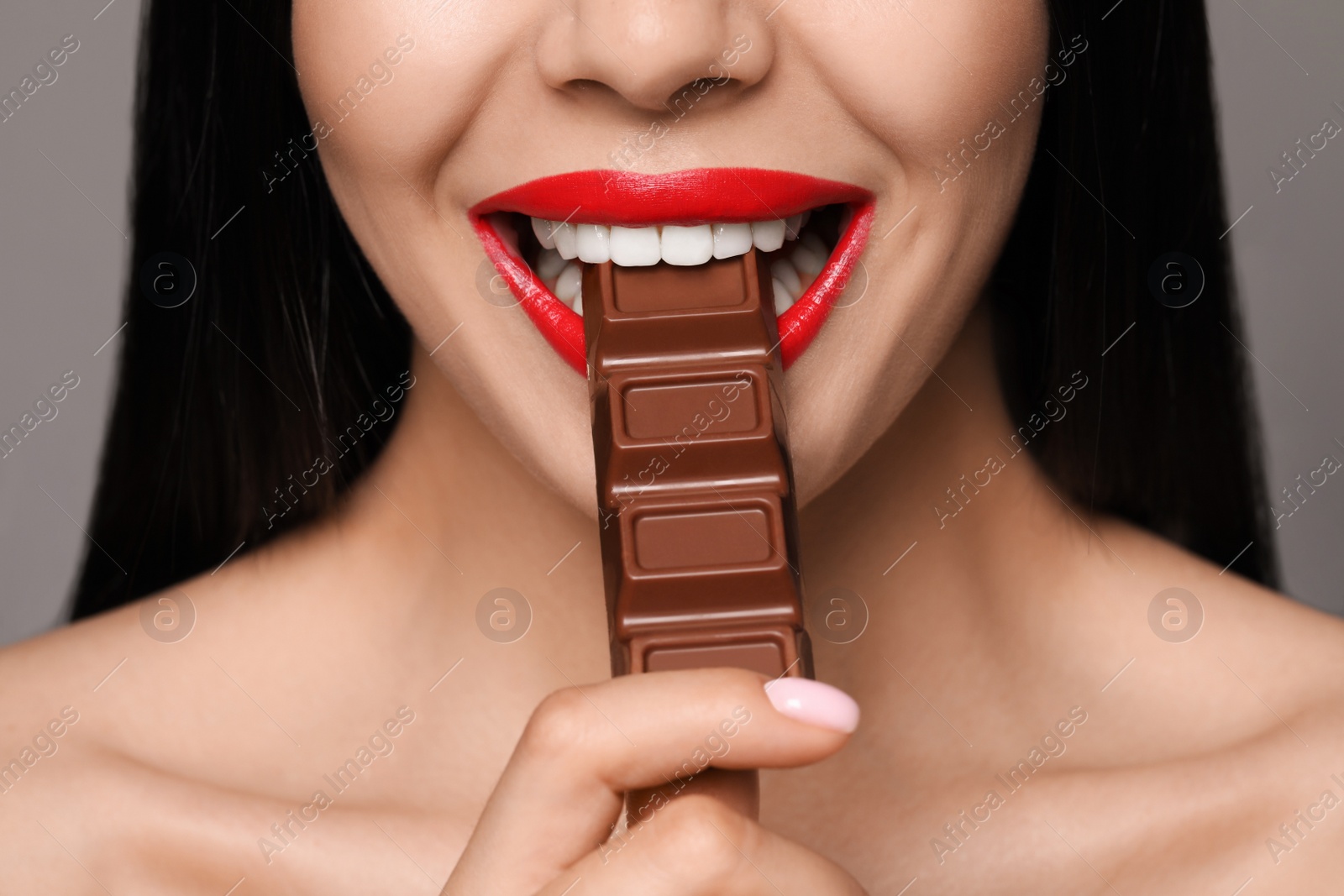 Photo of Young woman with red lips eating chocolate on grey background, closeup