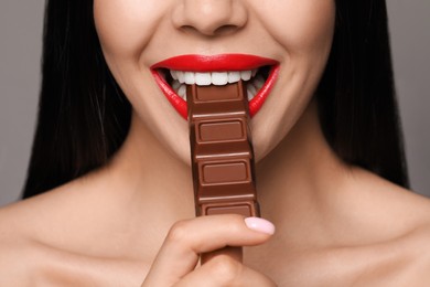 Photo of Young woman with red lips eating chocolate on grey background, closeup