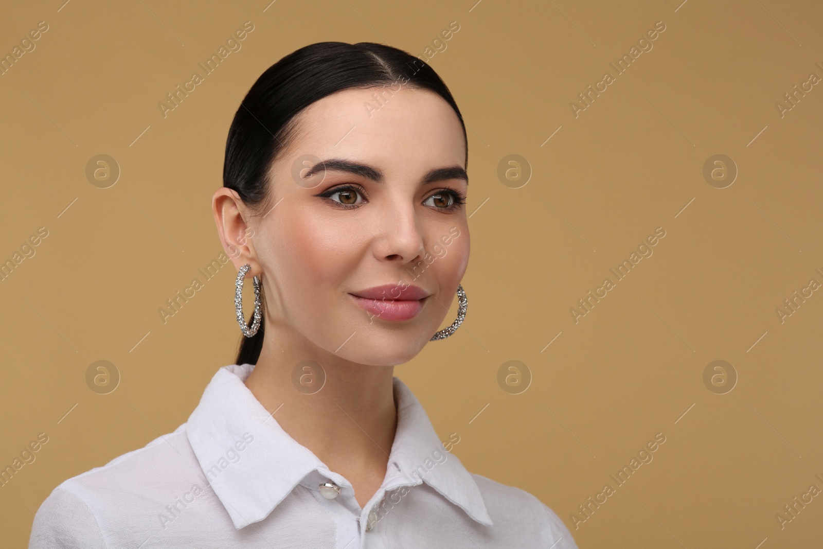 Photo of Beautiful young woman with elegant earrings on beige background