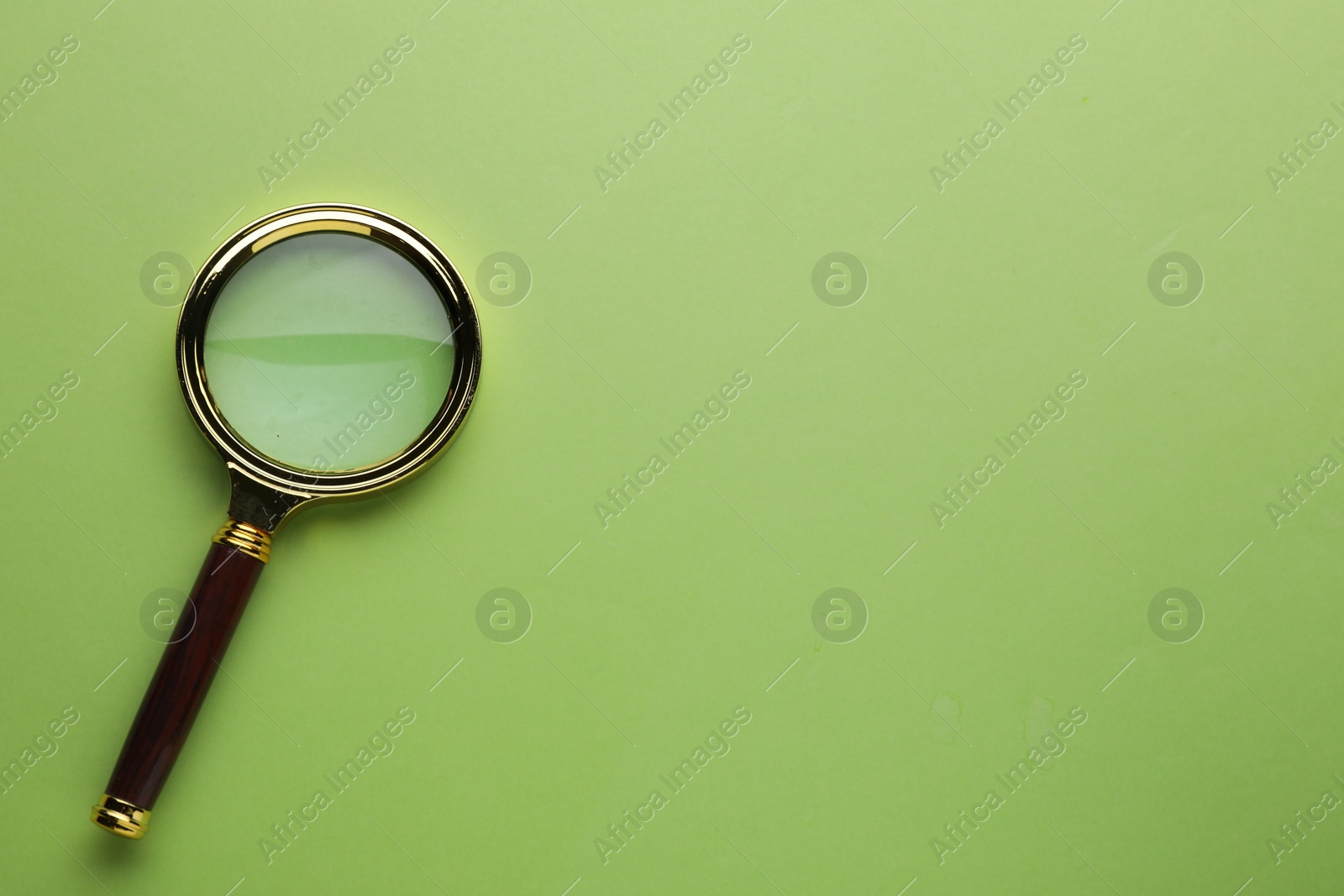 Photo of Magnifying glass on green background, top view. Space for text