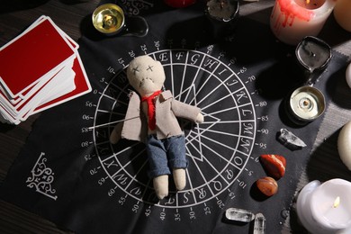 Photo of Voodoo doll pierced with needle surrounded by ceremonial items on table, flat lay. Curse ceremony