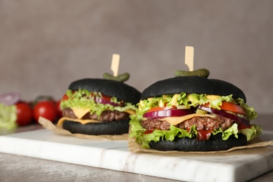 Board with black burgers on table against color background