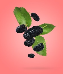 Image of Fresh ripe black mulberries and green leaves falling on coral color background