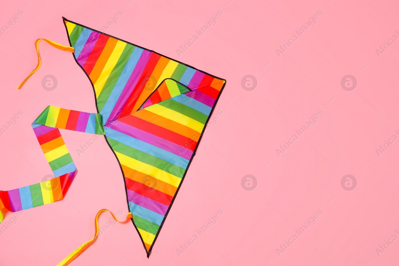 Photo of Bright rainbow kite on pink background, top view. Space for text