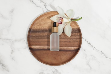 Bottle of cosmetic product and orchid flower on white marble table, top view