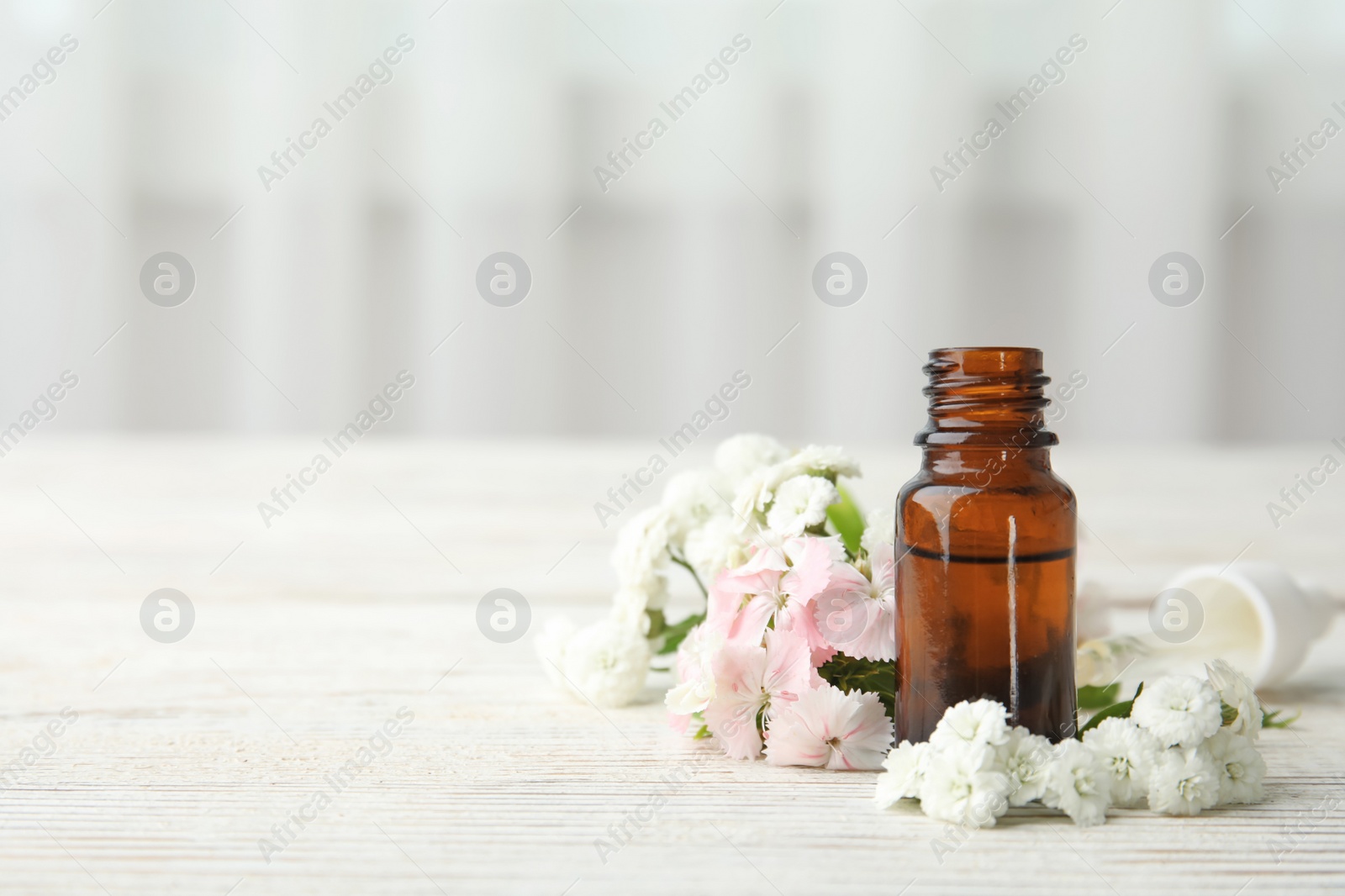 Photo of Bottle of essential oil and flowers on table