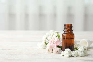 Bottle of essential oil and flowers on table