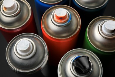 Photo of Cans of different graffiti spray paints on black background, closeup