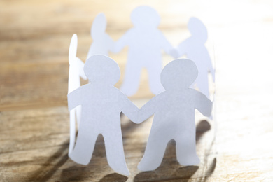 Photo of Paper people chain making circle on wooden background. Unity concept
