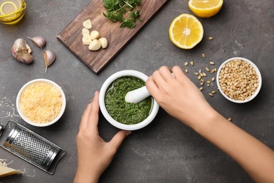 Woman preparing homemade basil pesto sauce on table, top view