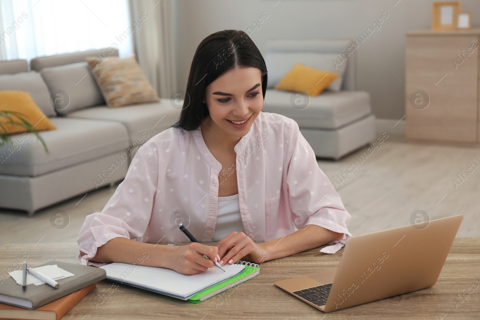 Photo of Young woman taking notes during online webinar at table indoors