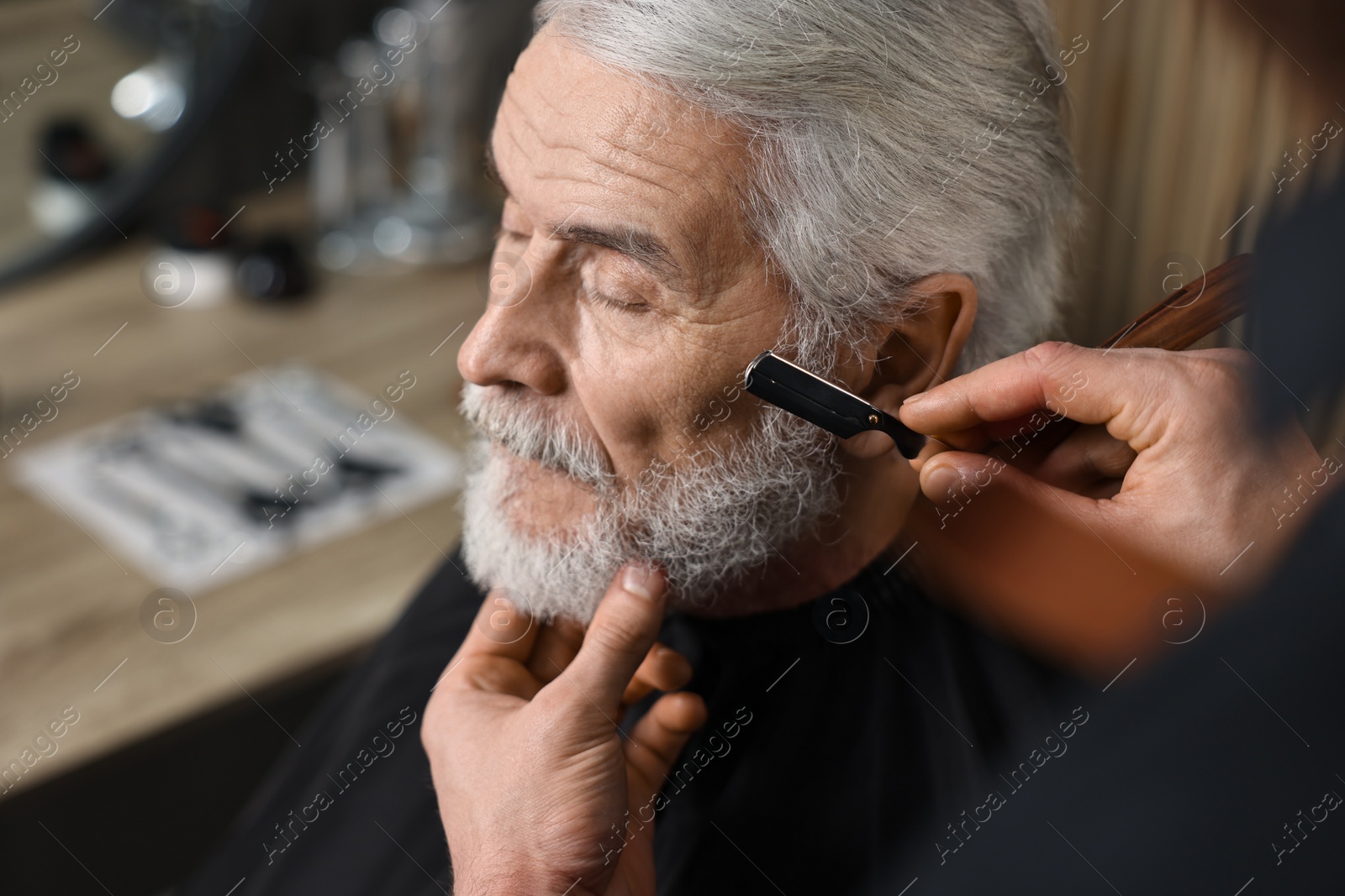Photo of Professional barber shaving client's beard with blade in barbershop, space for text