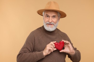 Photo of Senior man in hat with red decorative heart on beige background