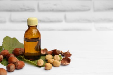 Photo of Bottle of hazelnut essential oil and nuts on white wooden table. Space for text