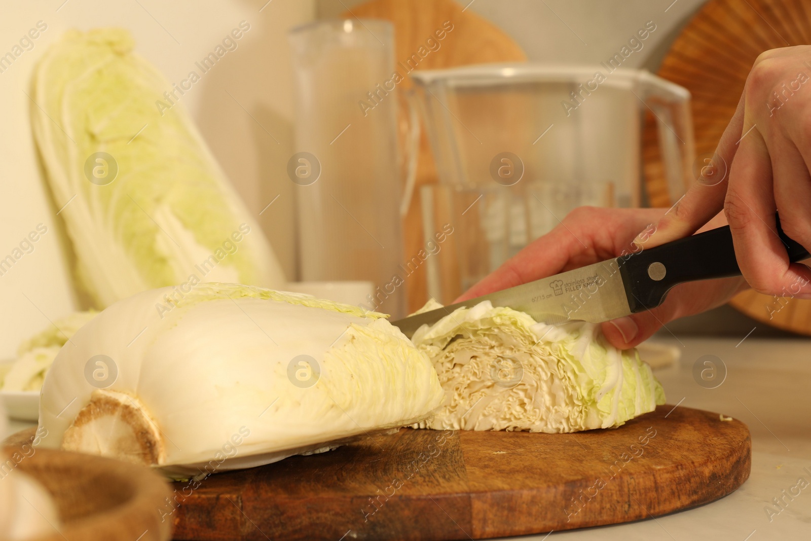 Photo of Woman cutting fresh chinese cabbage at kitchen table, closeup