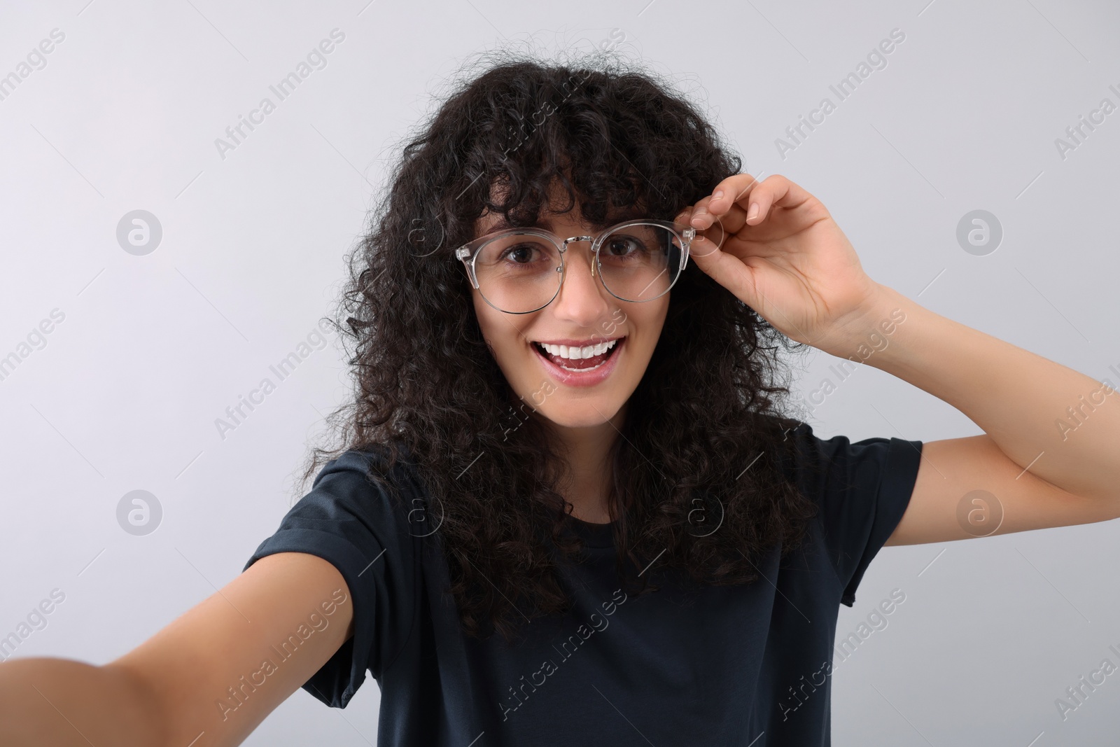 Photo of Beautiful young woman in eyeglasses taking selfie on light grey background