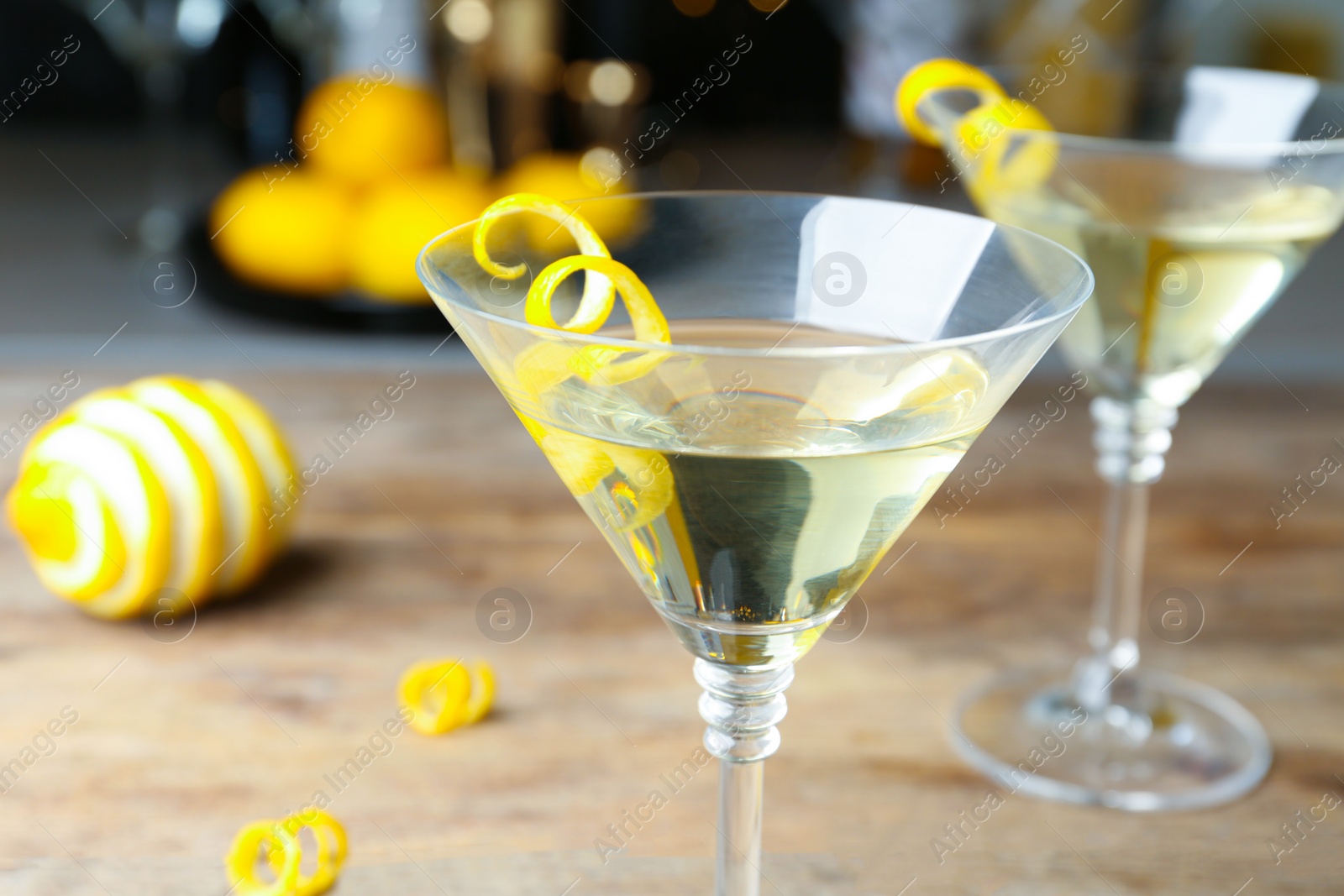 Photo of Glass of Lemon Drop Martini cocktail with zest on wooden table, closeup