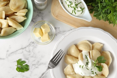 Photo of Delicious cooked dumplings with sour cream on white marble table, flat lay