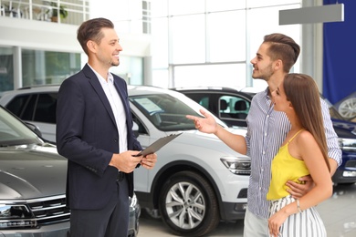Young couple choosing new car with salesman in salon