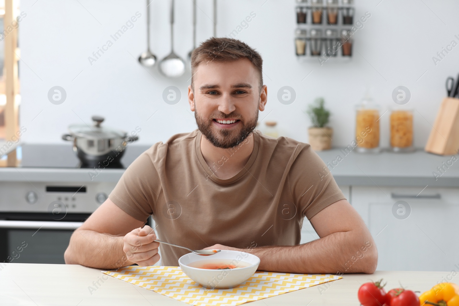 Photo of Young man eating tasty vegetable soup at table in kitchen