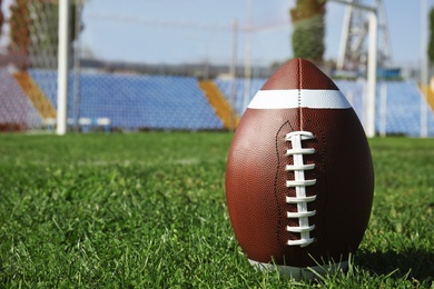 Photo of Ball on green field grass and space for text against net. American football match