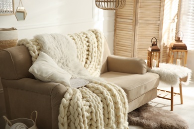 Photo of Cozy living room interior with beige sofa, knitted blanket and cushions