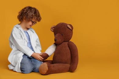 Photo of Little boy in medical uniform and toy bear with bandage on yellow background. Space for text