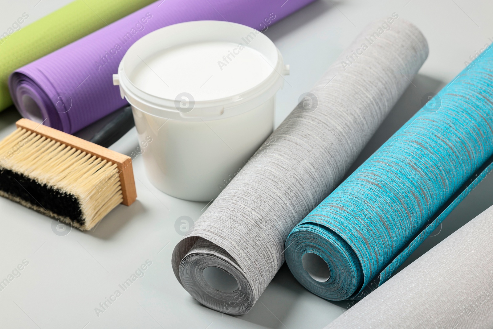 Photo of Different wallpaper rolls, brush and bucket with glue on light background