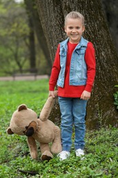 Photo of Cute little girl with teddy bear outdoors