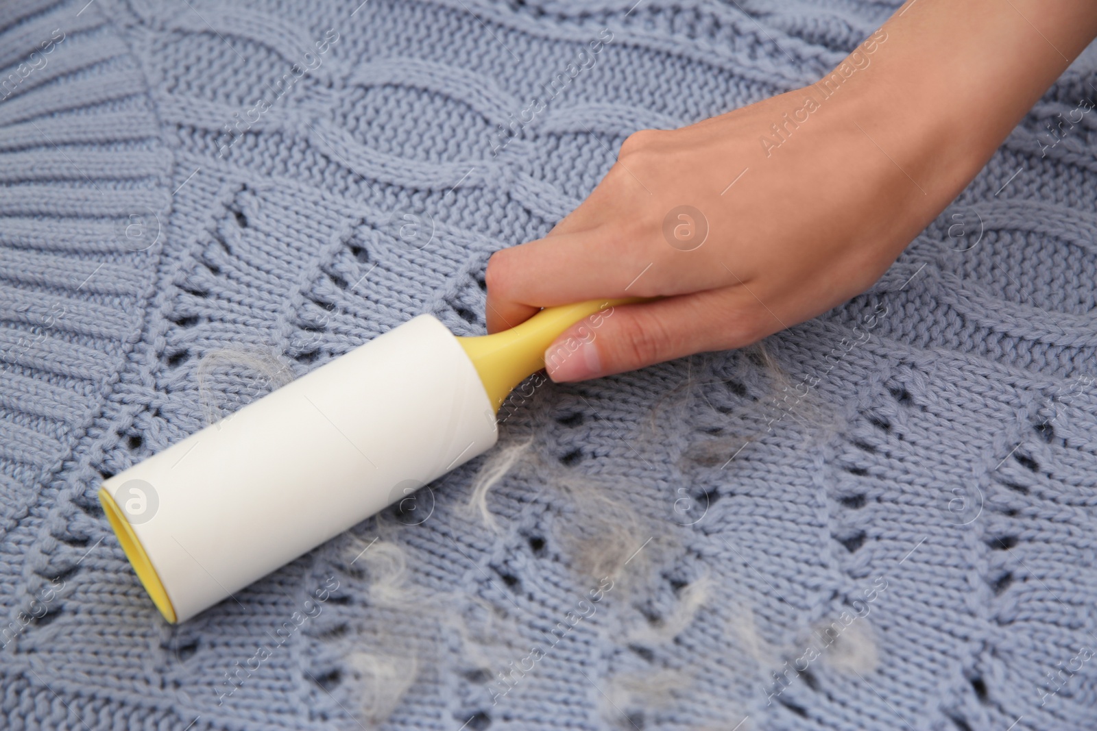 Photo of Woman removing hair from light blue knitted sweater with lint roller, closeup