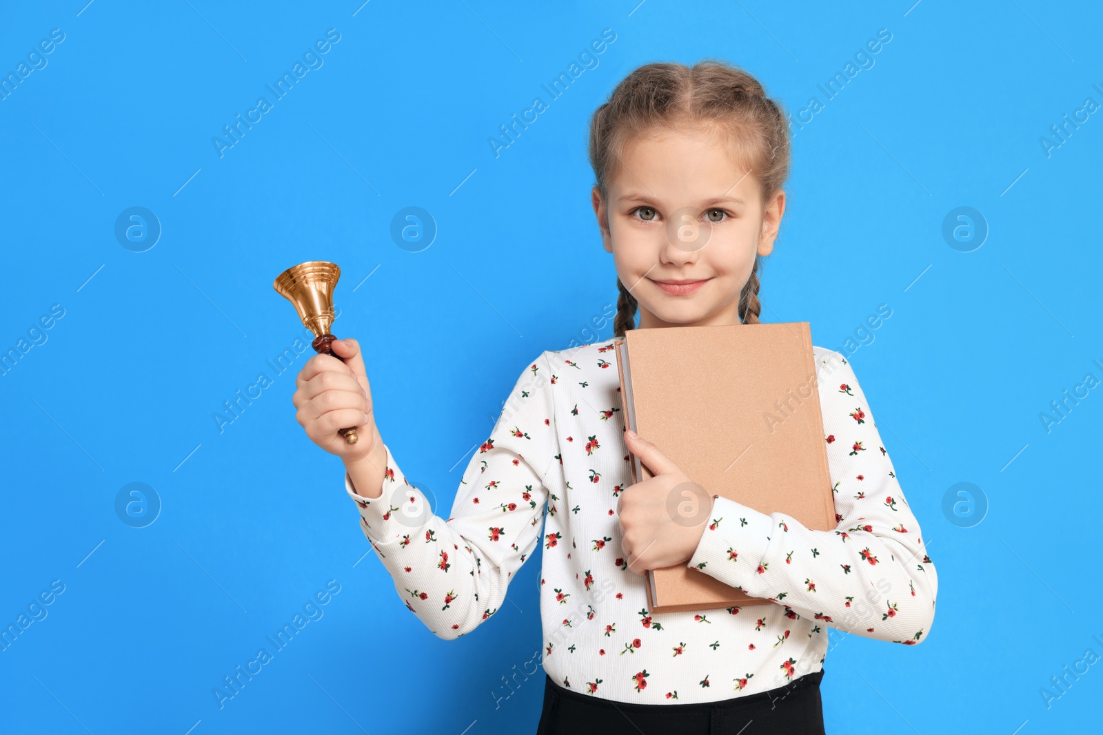 Photo of Pupil with school bell and book on light blue background