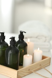 Wooden tray with soap dispensers and burning candles on white table