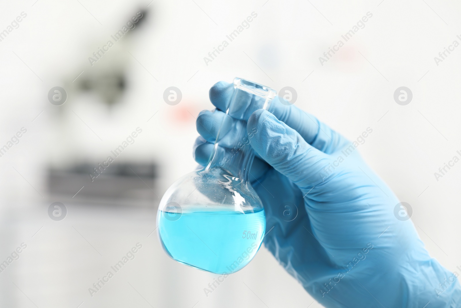 Photo of Scientist holding flask of light blue liquid in laboratory, closeup