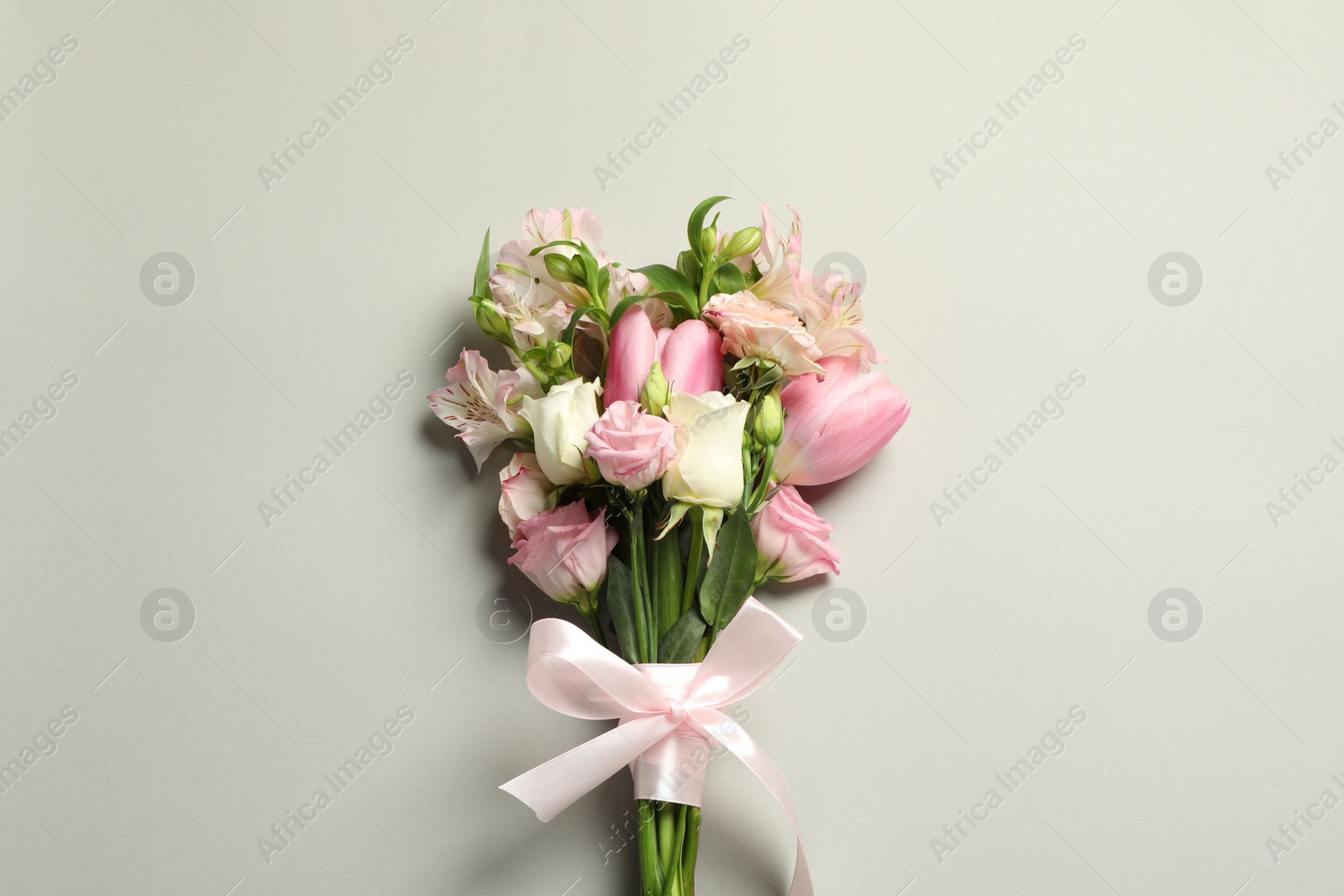 Photo of Happy Mother's Day. Bouquet of beautiful flowers tied with pink ribbon on light grey background, top view