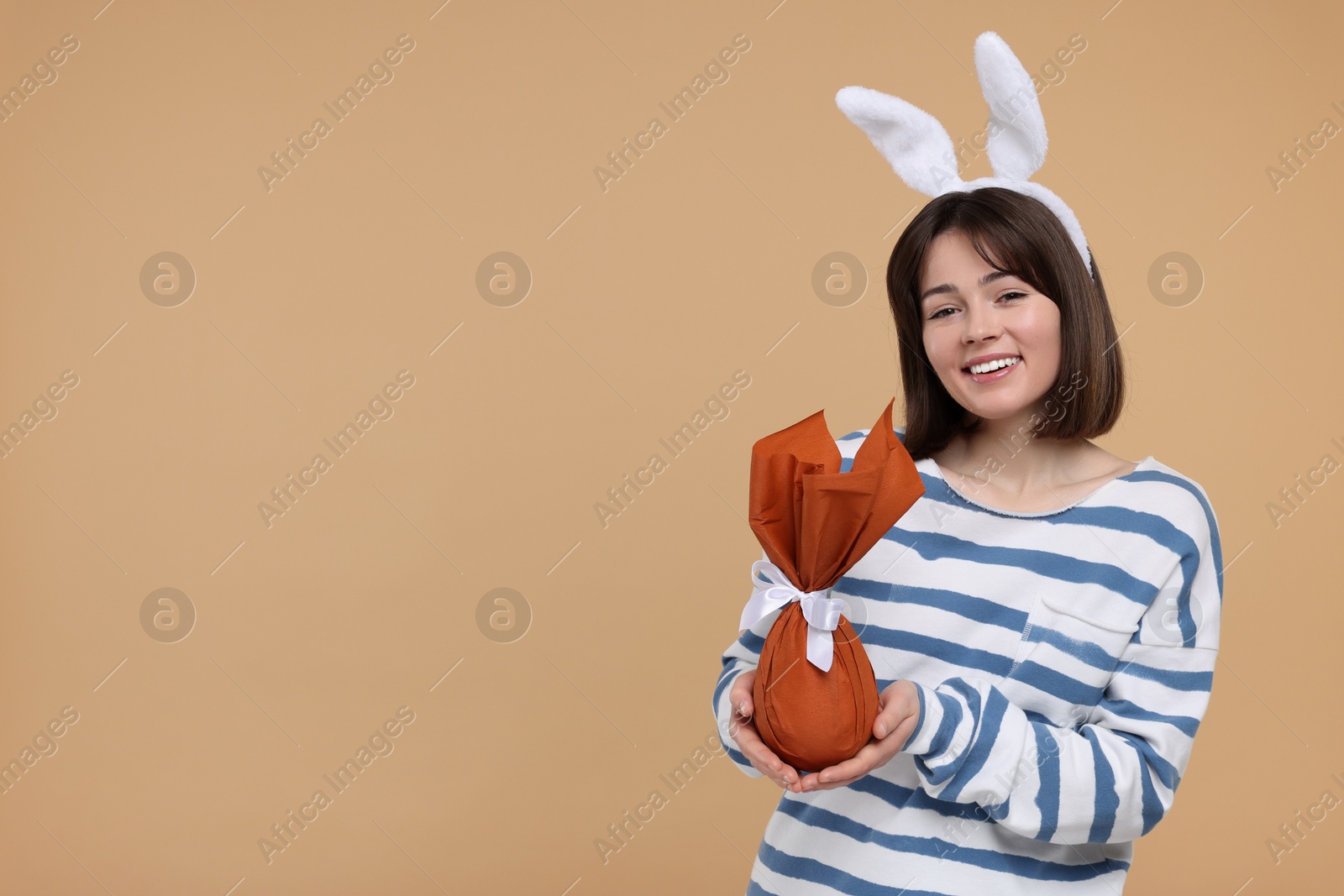 Photo of Easter celebration. Happy woman with bunny ears and wrapped egg on beige background, space for text