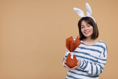 Easter celebration. Happy woman with bunny ears and wrapped egg on beige background, space for text