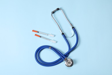 Stethoscope and syringes on light blue background, top view. Medical tools