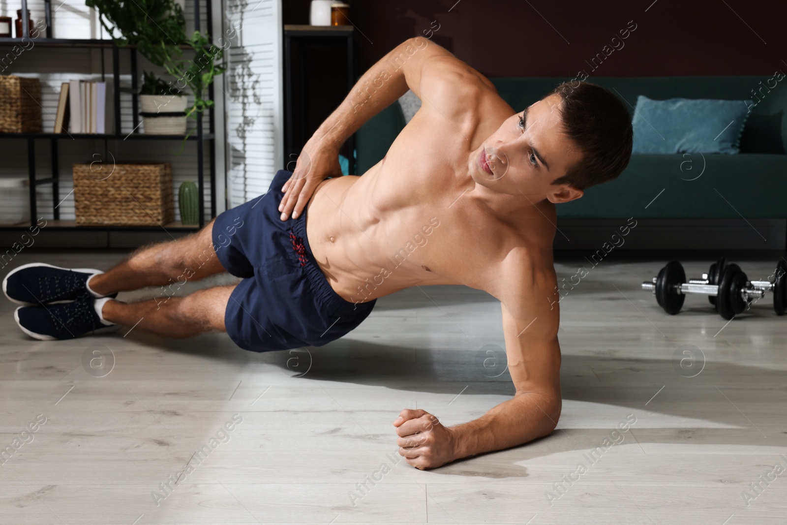 Photo of Handsome man doing side plank exercise on floor at home