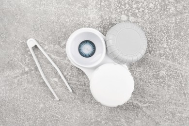 Photo of Case with color contact lenses and tweezers on light grey table, flat lay