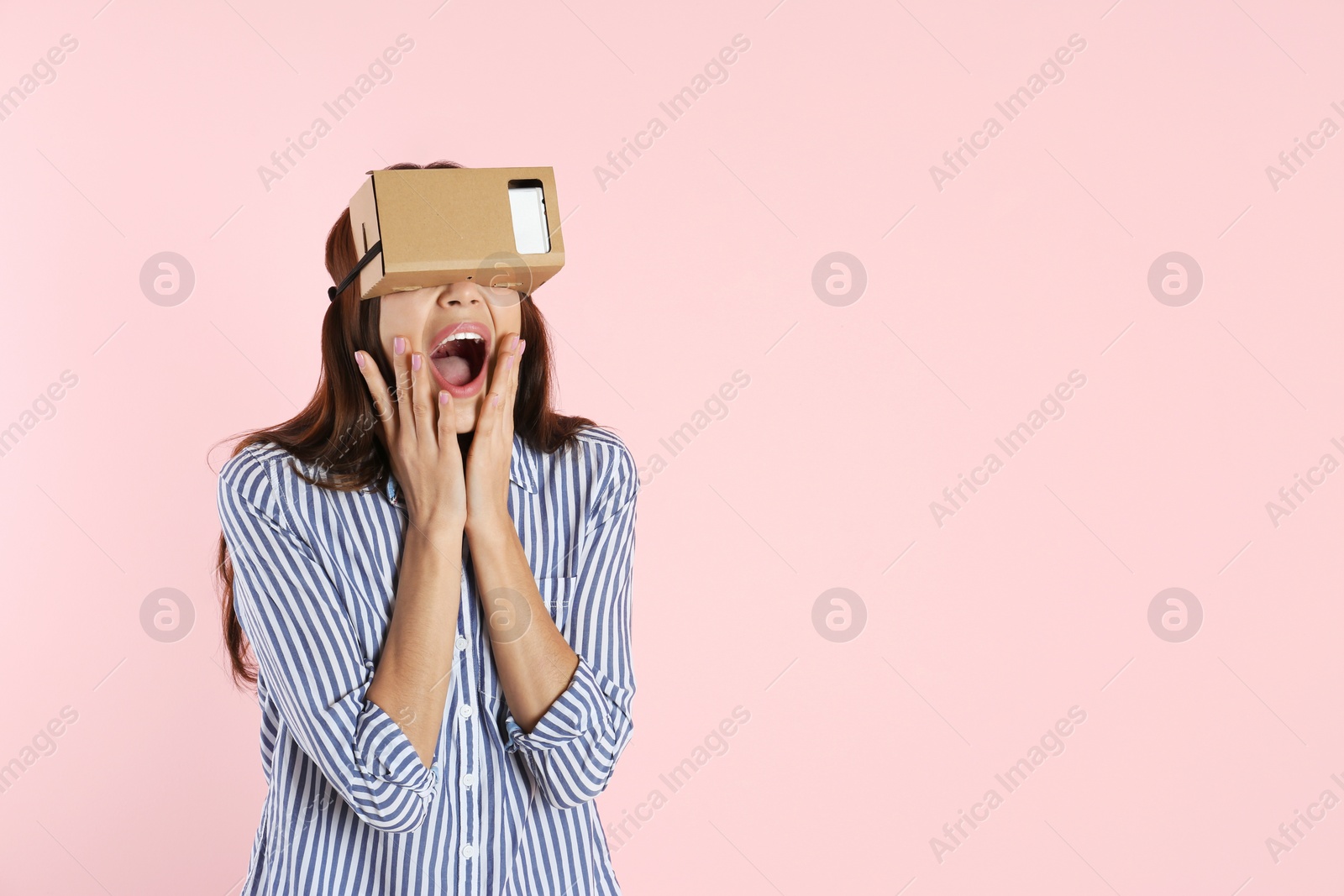 Photo of Young woman using cardboard virtual reality headset on color background. Space for text