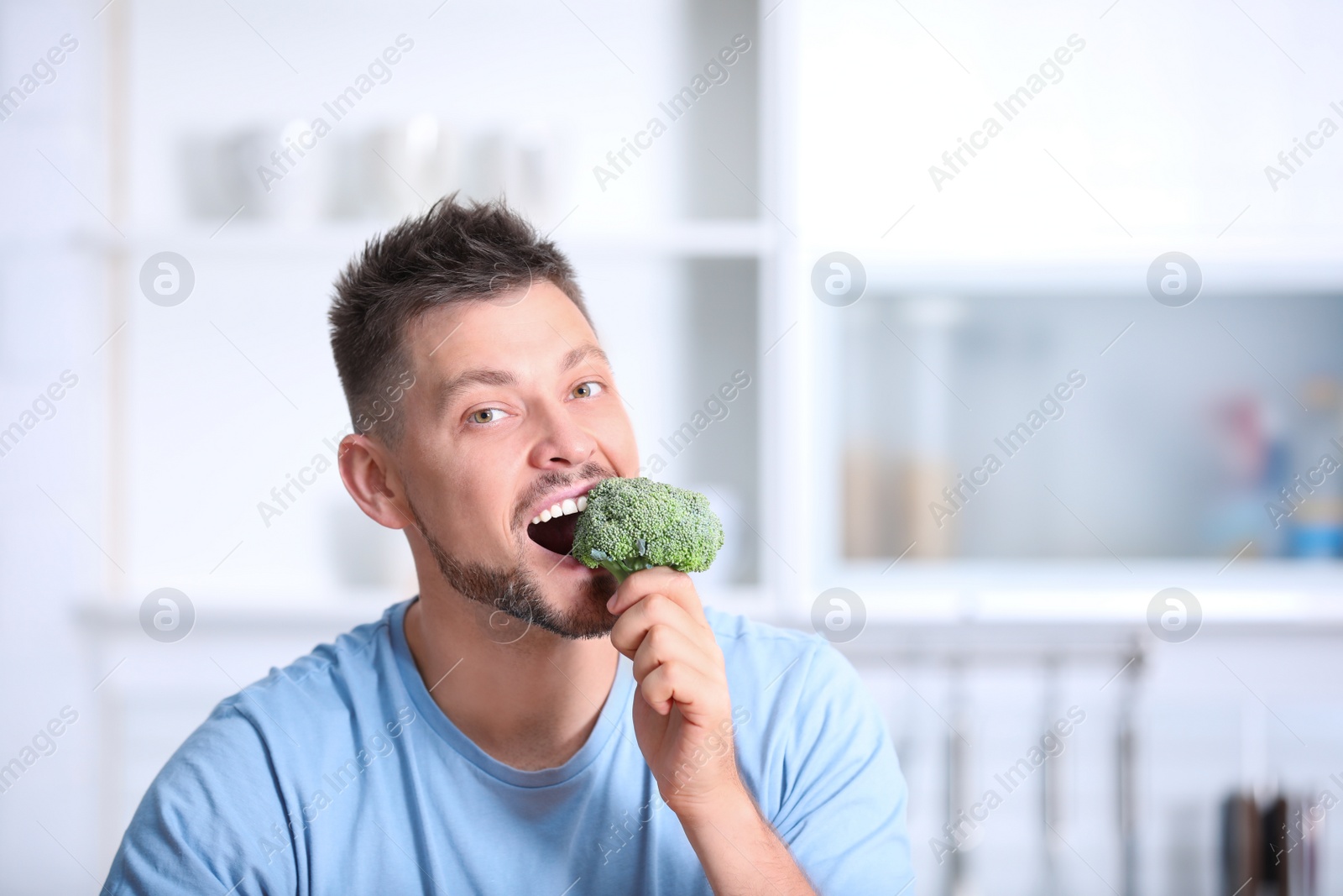 Photo of Portrait of happy man eating broccoli in kitchen