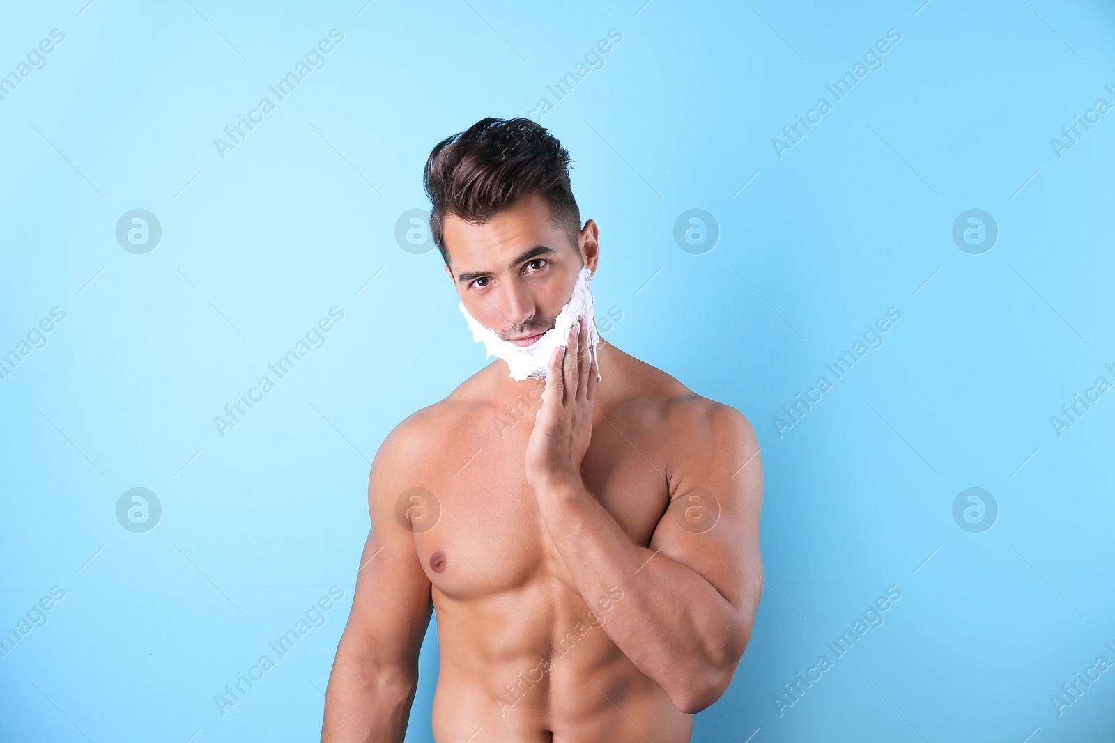 Photo of Handsome young man applying shaving foam on color background