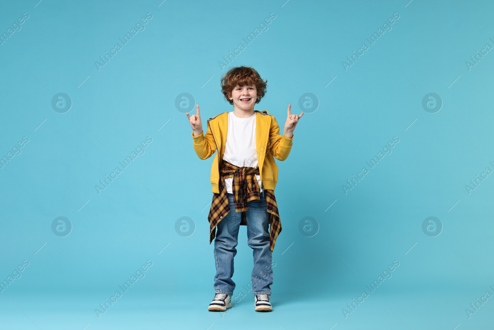 Photo of Happy little boy dancing on light blue background