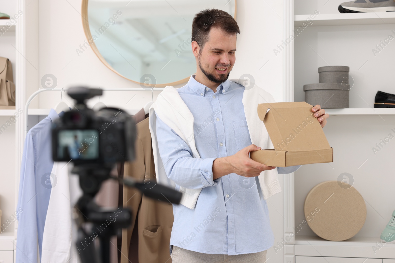 Photo of Smiling fashion blogger opening cardboard box while recording video at home