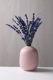 Bouquet of beautiful preserved lavender flowers on white table near grey wooden wall