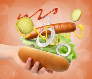 Image of Woman making hot dog on orange background, closeup. Ingredients levitating over bun