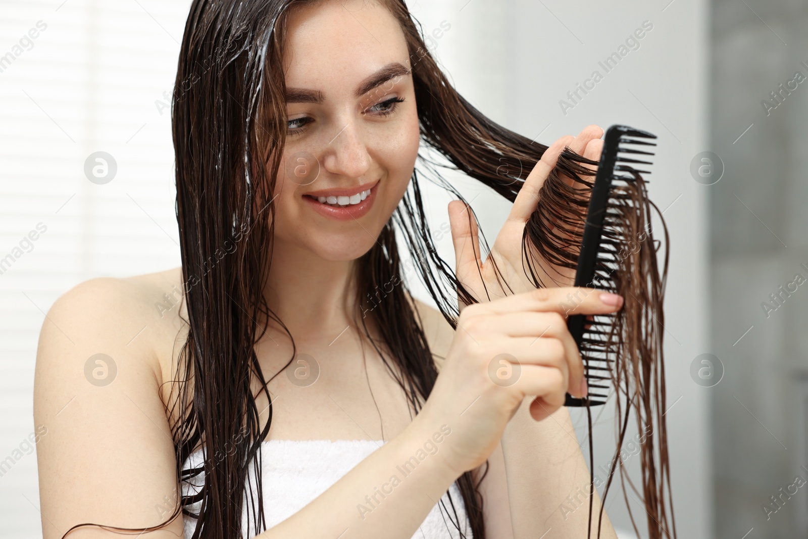 Photo of Young woman brushing hair after applying mask in bathroom