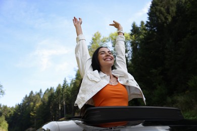 Enjoying trip. Happy woman leaning out of car roof outdoors